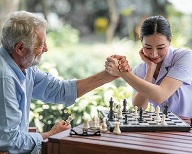 一个年轻的女人和一个年长的男人在外面下棋.